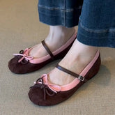 Brown flats with pink straps worn by a person on a beige carpet