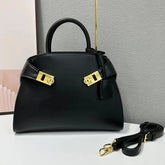 Black structured top-handle bag with gold turn-lock closure and detachable shoulder strap.