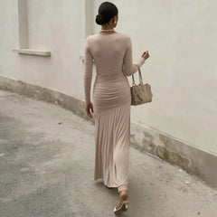 Woman in a long beige dress walking away from the camera against a plain wall.