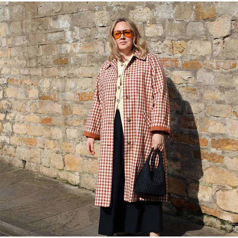 Woman wearing a checkered coat and sunglasses against a stone wall.
