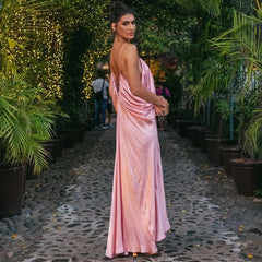 Woman in a pink dress standing among potted plants with string lights in the background