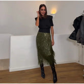 Woman wearing a black top and green sequin skirt in a room with white walls and wooden floor.