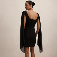 Woman wearing a black dress with a cape on a plain background