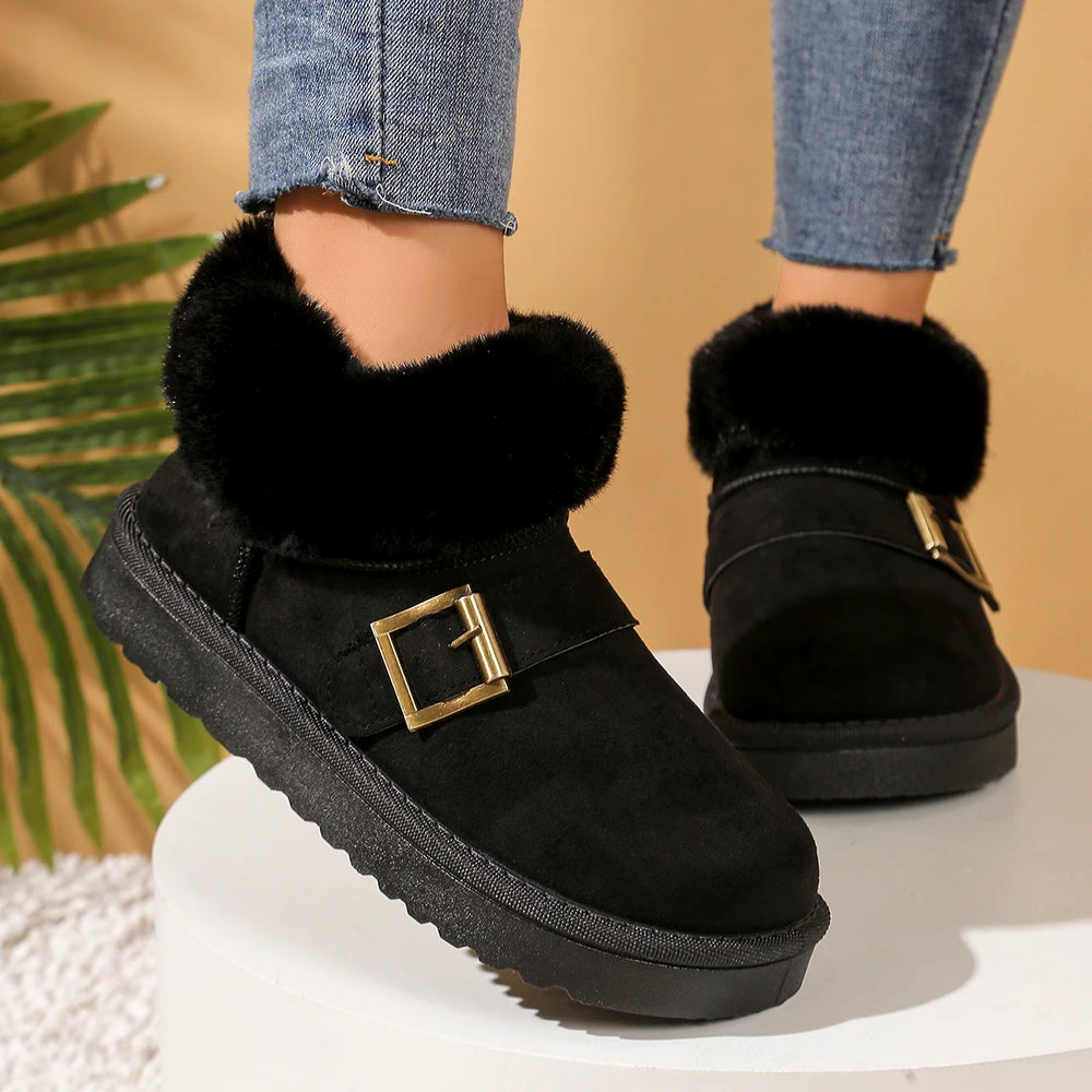 Black suede boots with fur trim and gold buckles on a neutral background