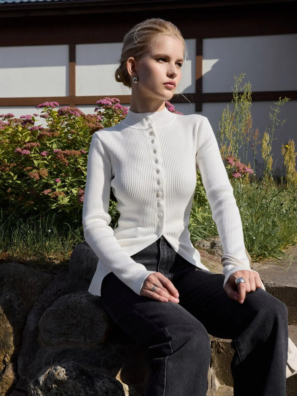 Woman wearing a white ribbed sweater and black pants sitting outdoors.