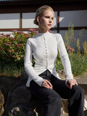Woman wearing a white ribbed sweater and black pants sitting outdoors.