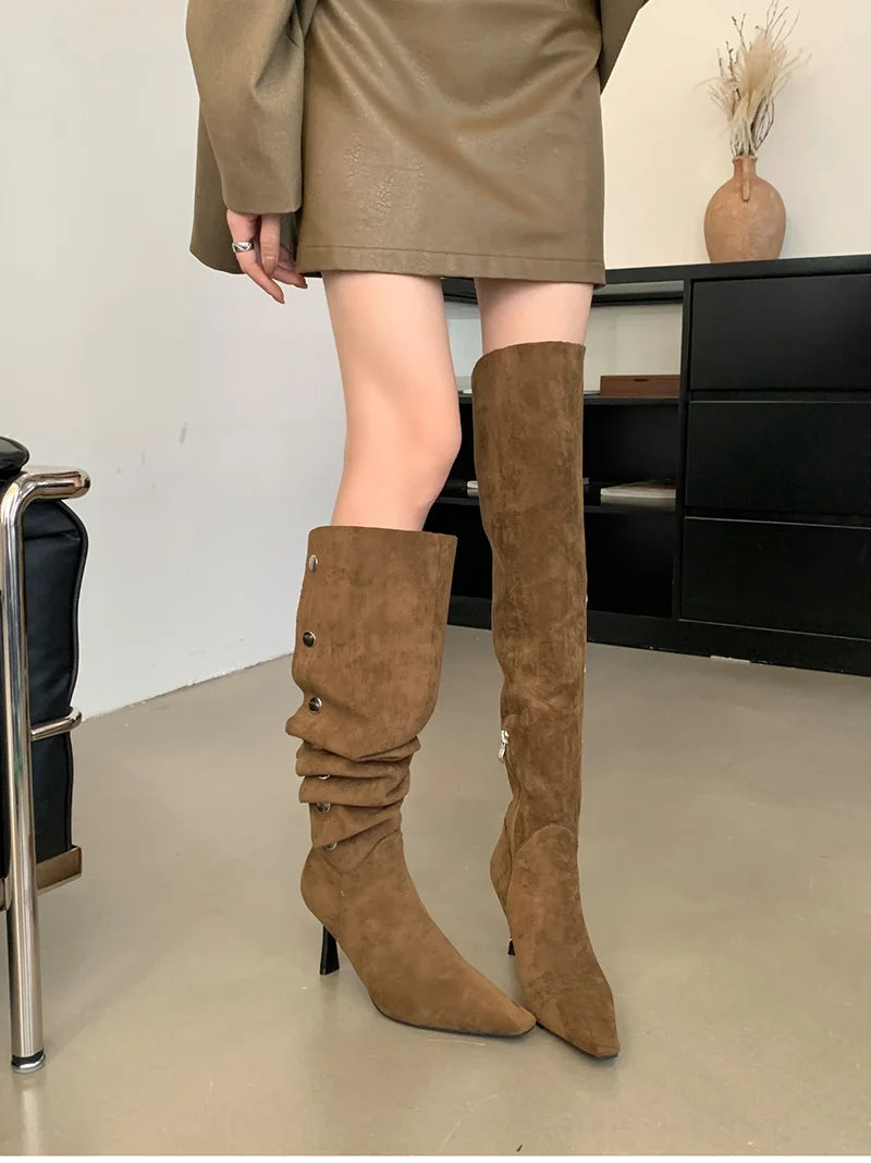Brown suede knee-high boots worn with a beige skirt indoors.