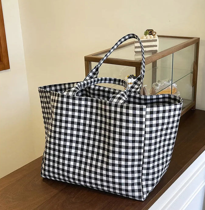 Black and white checkered tote bag on a wooden surface with a glass cabinet in the background.