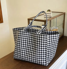 Black and white checkered tote bag on a wooden surface with a glass cabinet in the background.