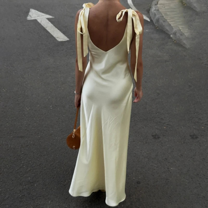Woman wearing a long, light-colored dress with ribbon straps on a street.