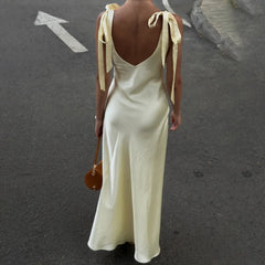 Woman wearing a long, light-colored dress with ribbon straps on a street.