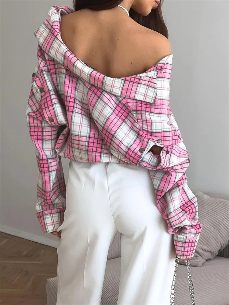 Person wearing a pink and white plaid shirt over a white top, standing against a neutral background.