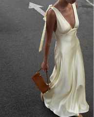 Woman in a white dress holding a brown handbag on a street.