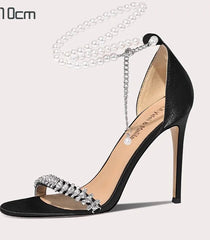 Black high-heeled shoe with decorative chain on a light gray background