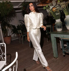 Woman in a white suit standing in an indoor setting with plants and furniture.