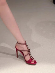 Side view of a stiletto sandal with red silk upper and crystal embellishments on a light background.