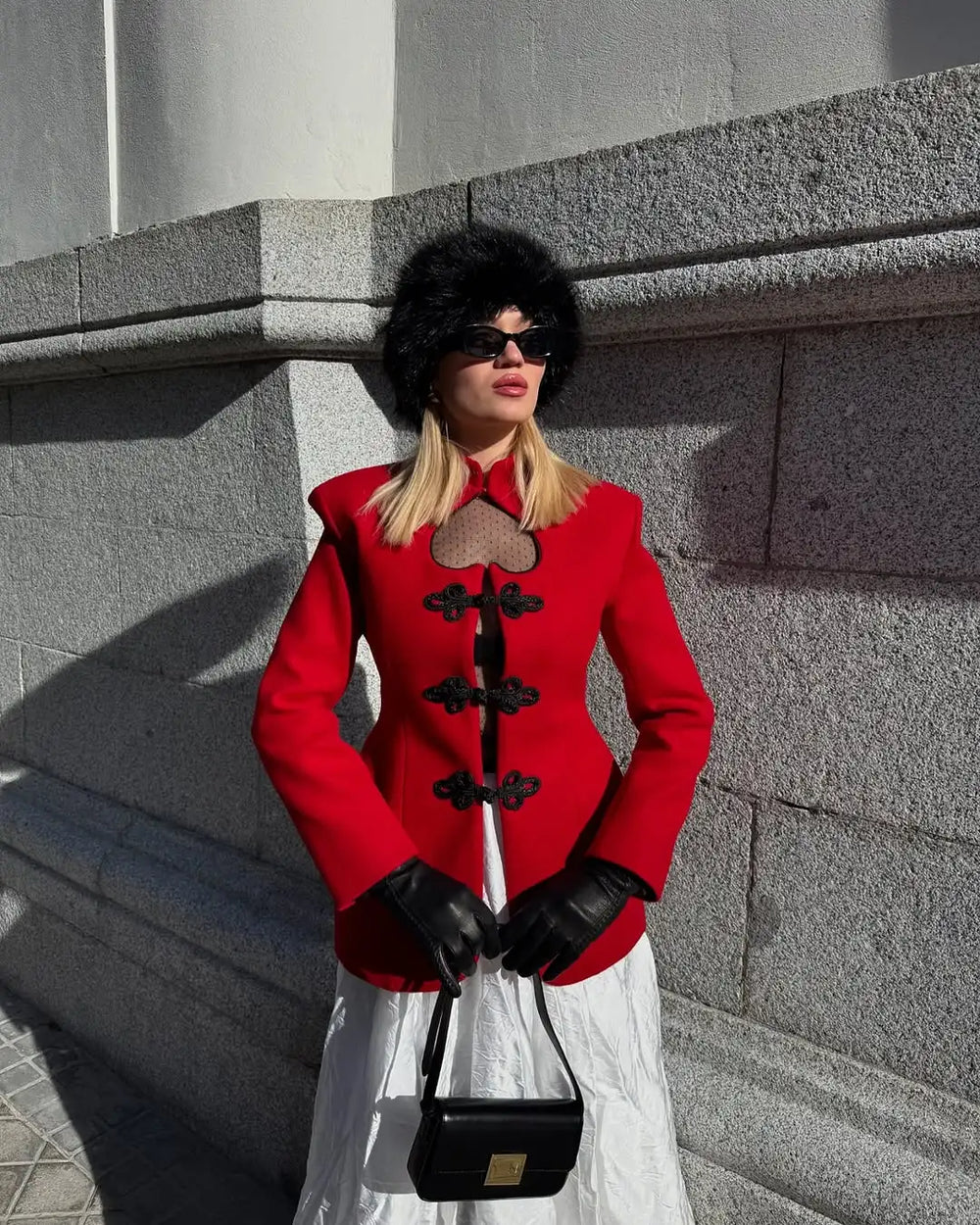 Woman in a red jacket with black accents standing against a gray stone wall.
