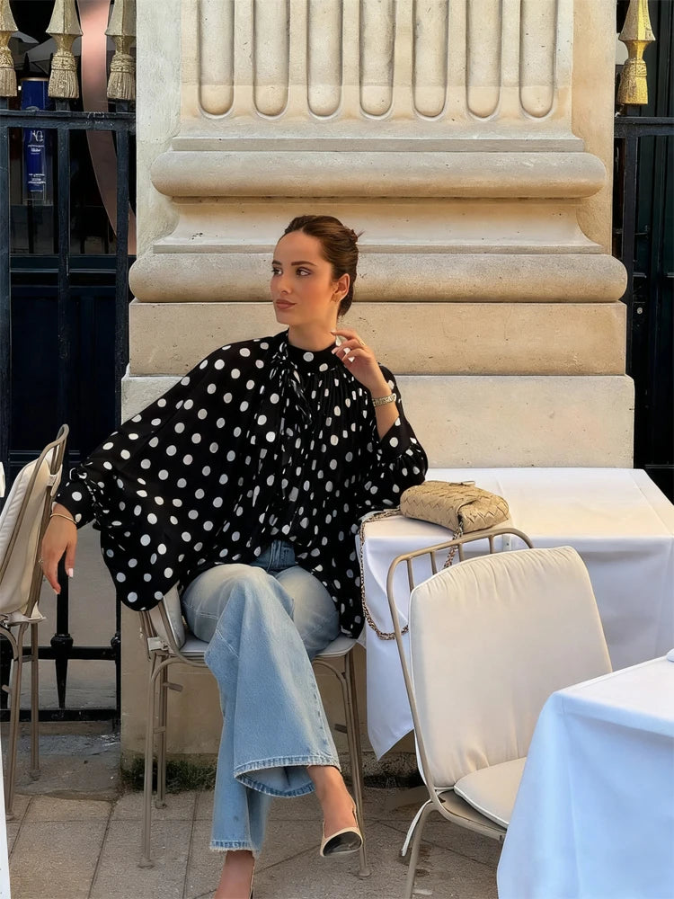 Woman sitting at an outdoor cafe table with a polka dot blouse and jeans.