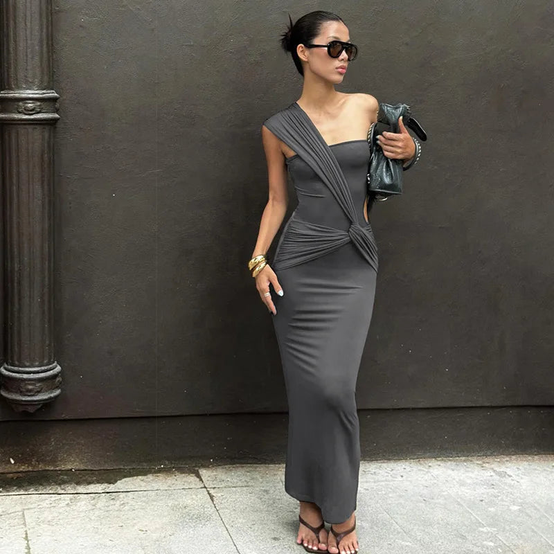 Woman in a gray dress standing against a dark wall.