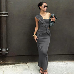 Woman in a gray dress standing against a dark wall.