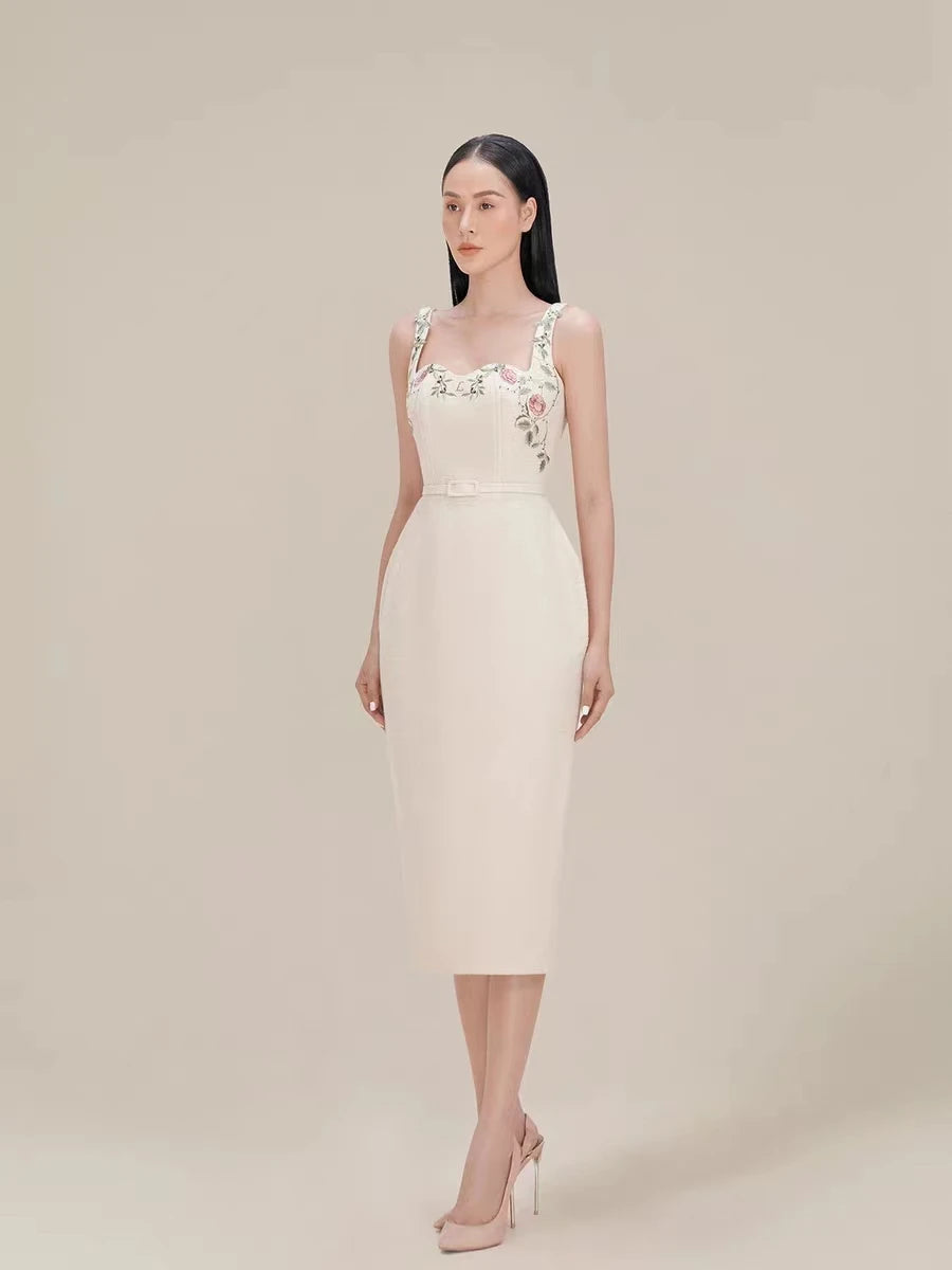 Woman wearing a light-colored dress with floral embellishments on a plain background