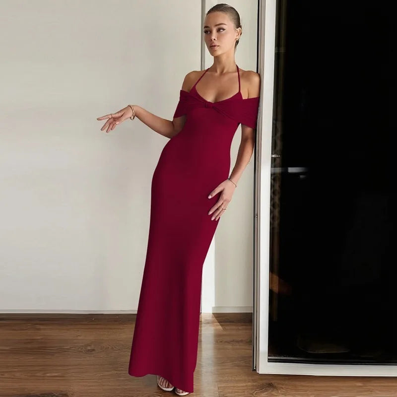 Woman in a burgundy evening gown standing against a neutral wall.