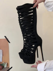 Black high-heeled boot with criss-cross design held by a person against a neutral background