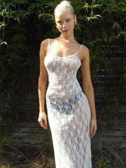 Woman wearing a white lace dress standing outdoors with greenery in the background