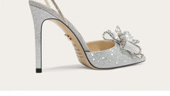 Silver glitter high-heeled shoe with a decorative bow on a light gray background
