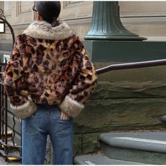 Person wearing a leopard print jacket with fur trim standing against a stone wall.