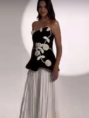 Woman wearing a black one-shoulder dress with white floral embroidery on a plain background