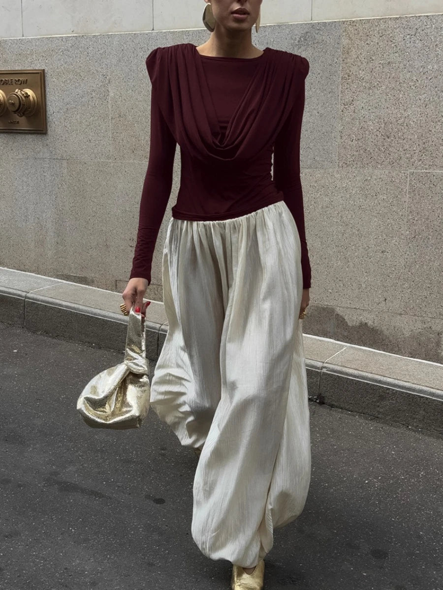 Person wearing a burgundy top and white pants against a stone wall.