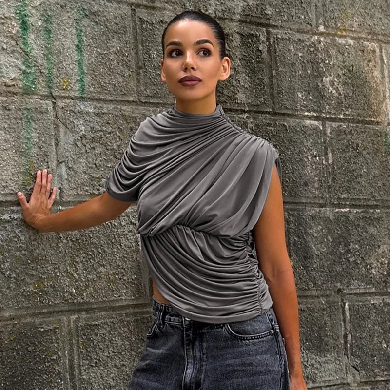 Woman wearing a gray draped top and jeans against a textured wall.