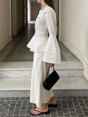 Person wearing a white outfit with bell sleeves in an indoor setting