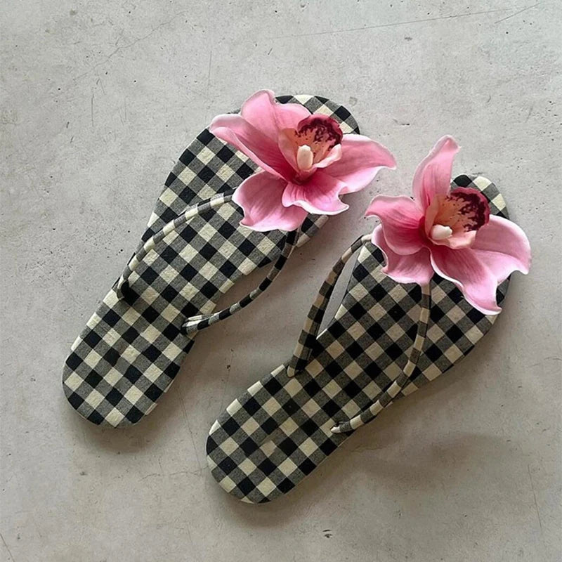 Checkered flip-flops with pink flowers on a concrete surface