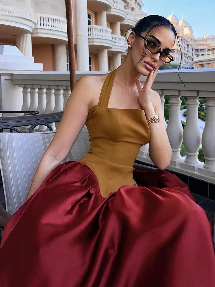 Woman in a gold and red dress posing on a balcony with a cityscape background