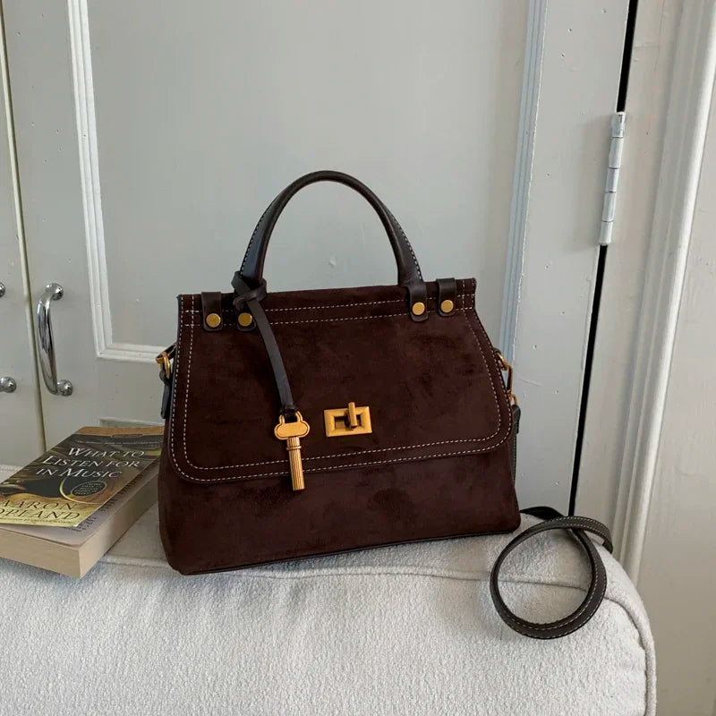 Brown handbag with a gold lock on a textured surface with a book in the background.