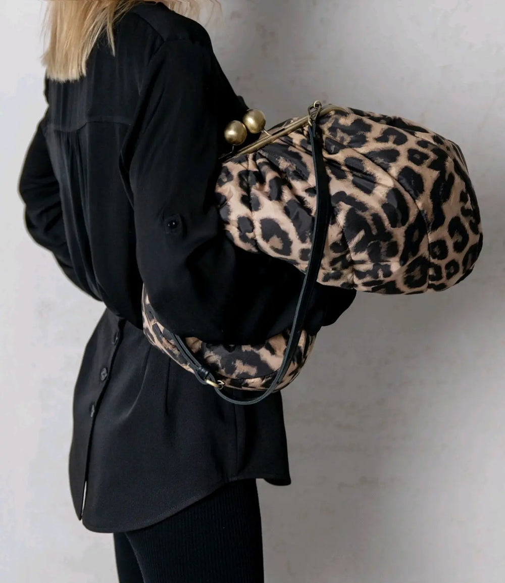 Person wearing a black coat with a leopard print bag over their shoulder against a plain background