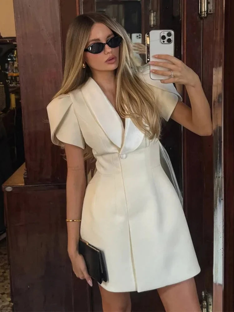 Three-quarter view showing puff sleeves and the clean A-line mini shape, styled with a small white handbag indoors.