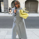 Mirror selfie on a city street wearing a long grey coat with asymmetric buttons, sunglasses, and a bright yellow tote.