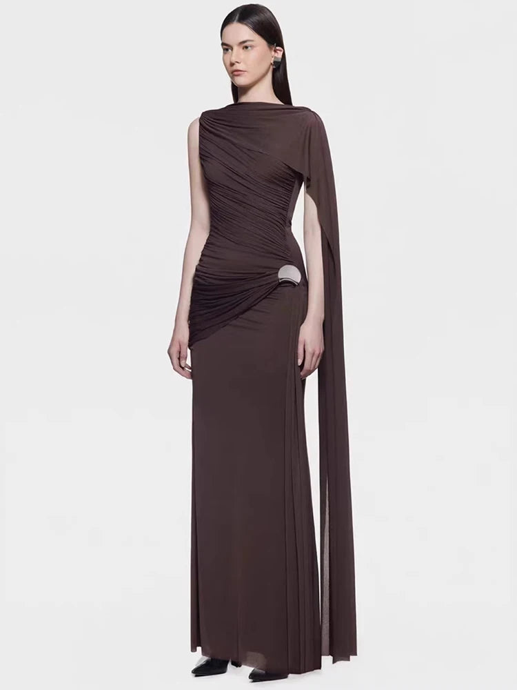 Model wearing a deep brown asymmetrical cape sleeve maxi gown, standing on a white background with a sleek, elongated formal silhouette.