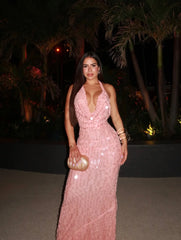 Woman in a backless, floor-length dress with lace-up detail and sparkle, standing outdoors at night with palm trees in the background