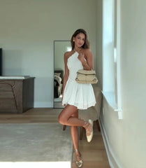 Woman in a white dress holding a beige handbag in a room with neutral decor.