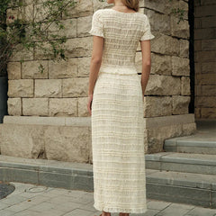 Backside view of a woman wearing a cropped top paired with a high-waisted maxi skirt for beachwear, standing in front of a stone wall.