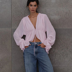 Woman wearing a light pink V-neck blouse styled casually with denim jeans against a grey background