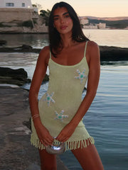 A woman in a pearl-embellished starfish detail on a green mini dress standing by a waterfront.