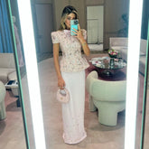 Mirror selfie indoors showing a pink beaded short-sleeve top paired with an ivory floor-length skirt and a small matching handbag.