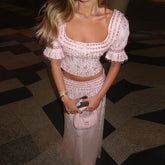 Model in a pink embellished two-piece set indoors, featuring a square neckline, fitted bodice, and floor-length skirt with sparkle.