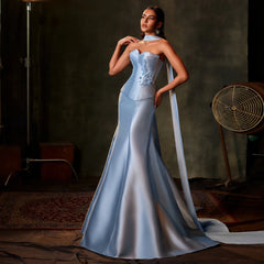Woman in a light blue evening gown standing in a dimly lit room.
