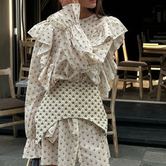 A woman wearing a belted mini dress with a floral print in an indoor setting.